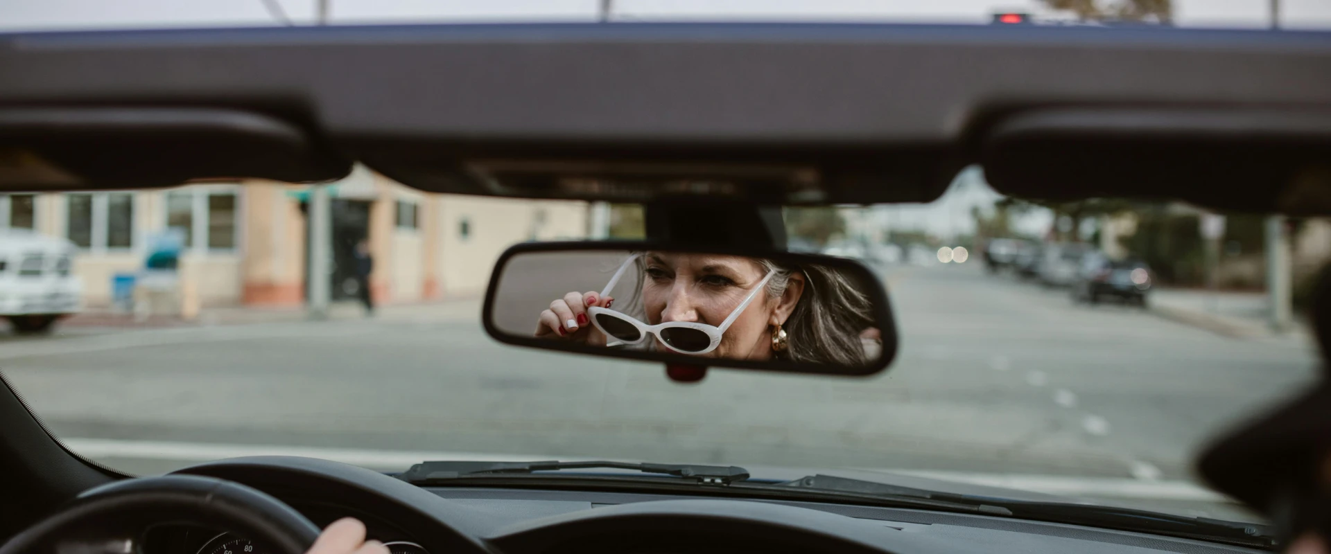 A photo of a woman in a car holding a pair of sunglasses.